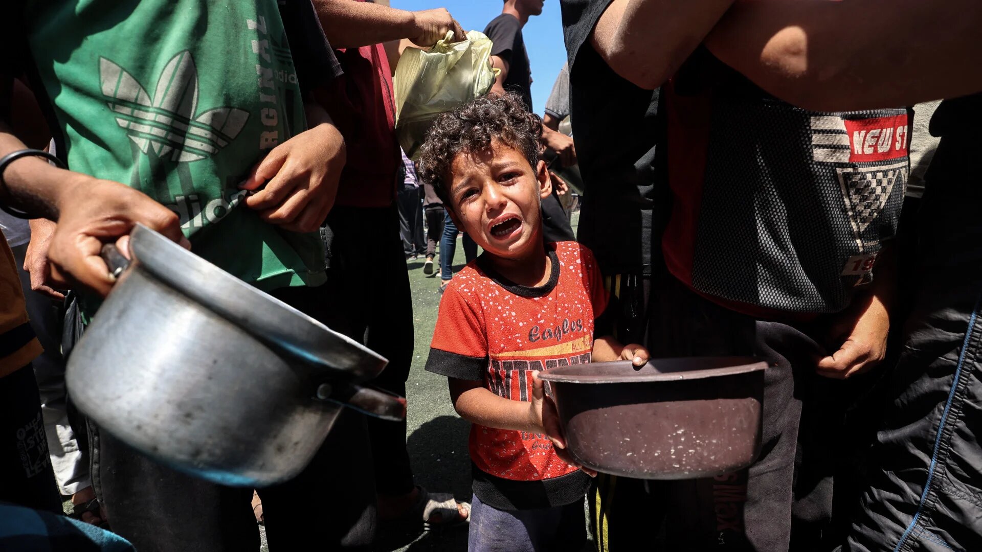 A child cries as Palestinians queue for food at a distribution point in Nuseirat refugee camp, central Gaza, on 24 May 2025. (Eyad Baba/AFP)