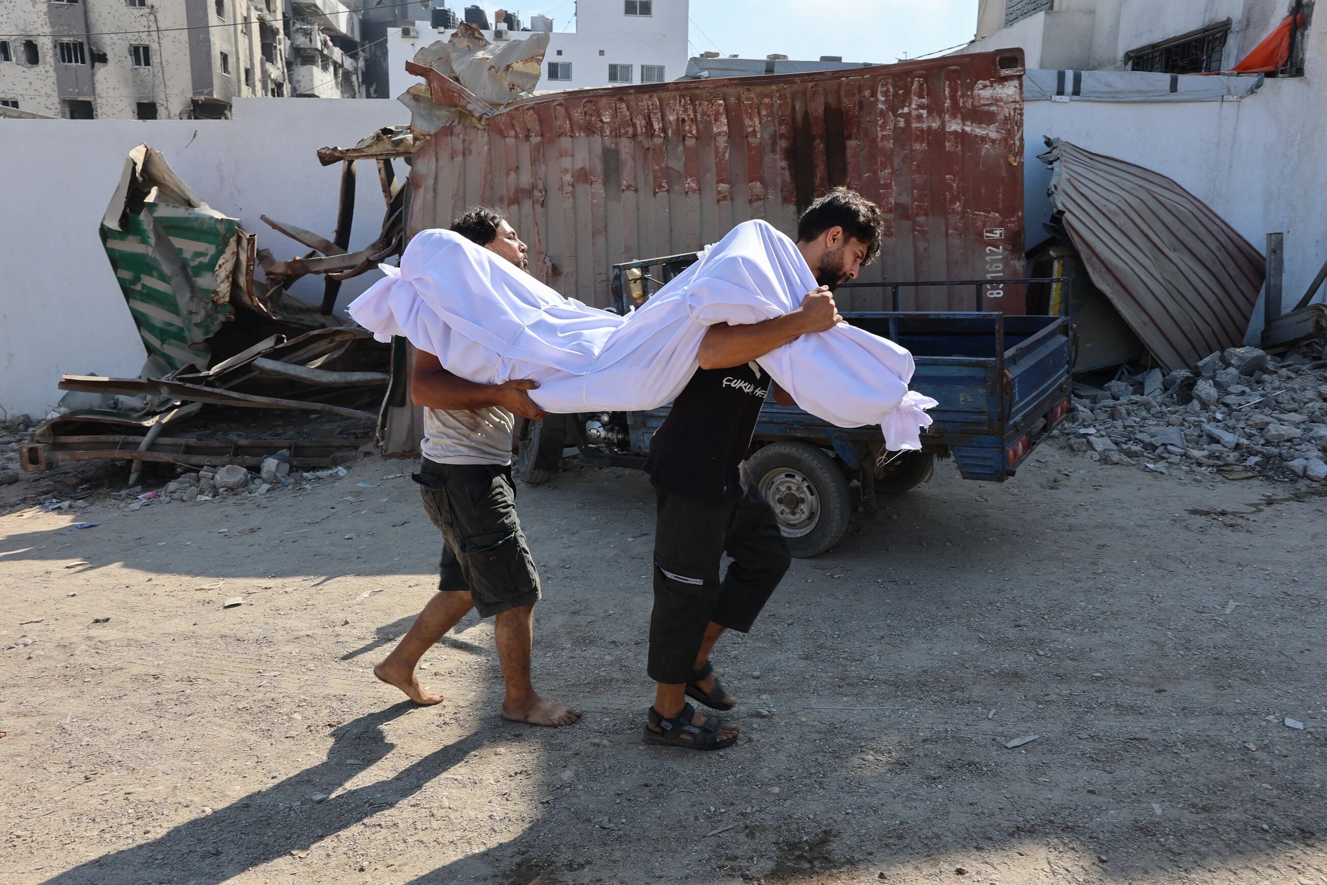 Palestinian men carry the body of a person killed while waiting for aid outside al-Shifa Hospital in Gaza City on 3 July 2025 (Omar al-Qattaa/AFP)