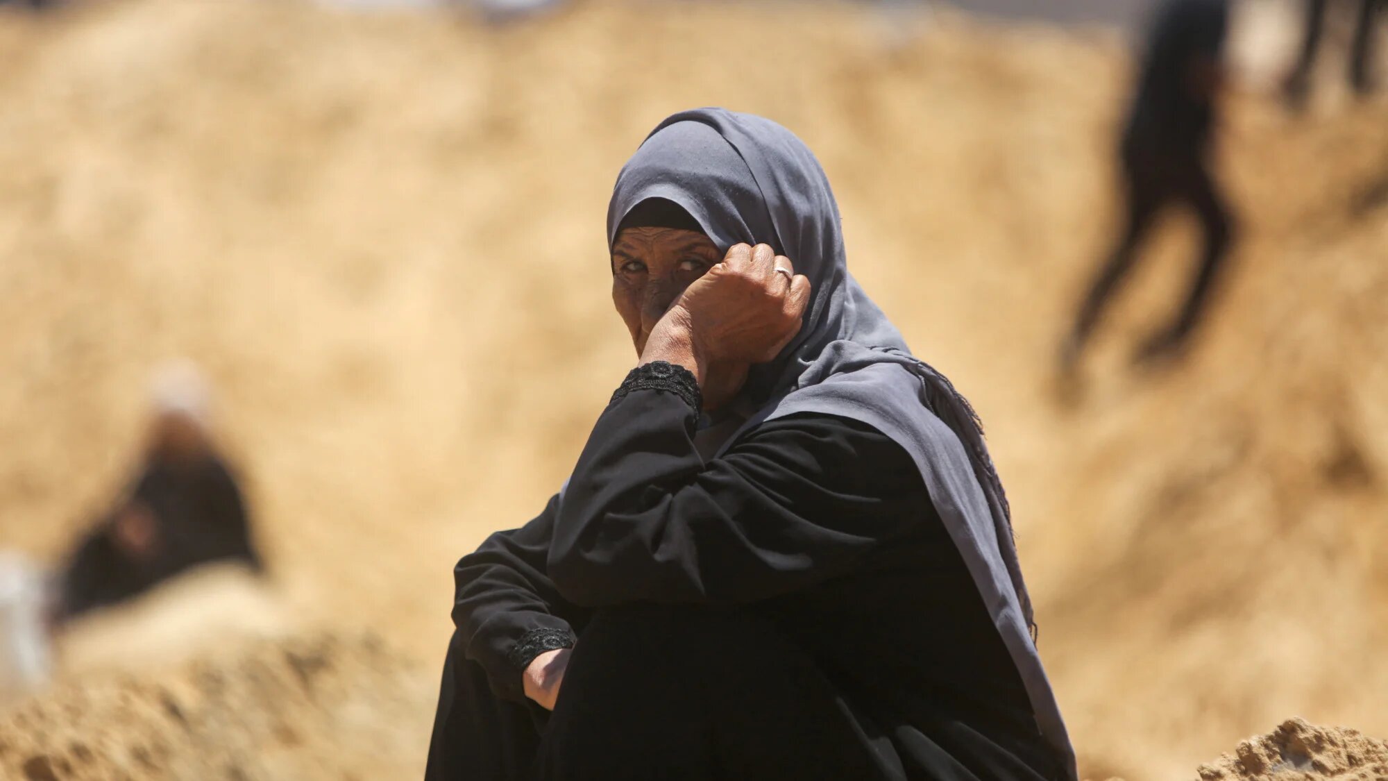 A woman looks on as Palestinians inspect destroyed tents by Israeli forces at a makeshift displacement camp in Khan Yunis in the southern Gaza strip on 11 July 2025 (AFP)