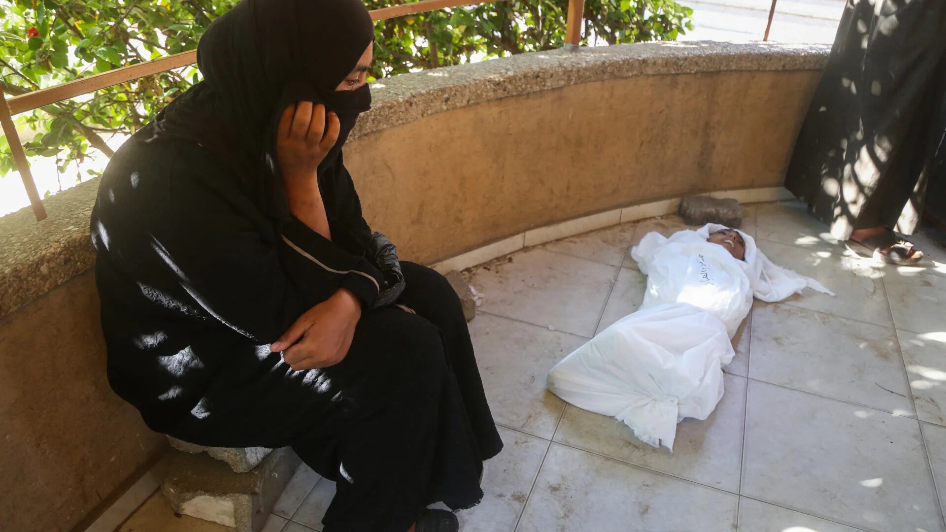 The mother of 14-year-old Palestinian Abdul Jawad al-Ghalban, who died of starvation, mourns beside his shrouded body at Nasser Hospital in Khan Younis, southern Gaza Strip, on 22 July 2025 (AFP)
