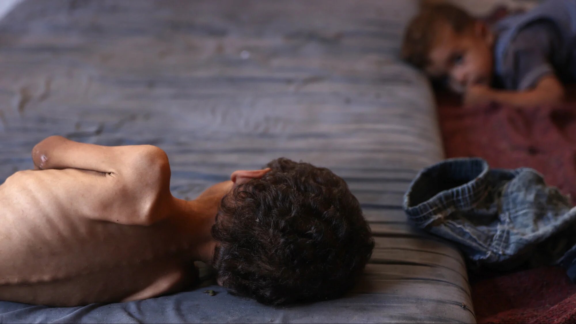 Yazan, a malnourished 2-year-old Palestinian boy, lays on a mattress next to his brother at their family's damaged home in the Al-Shati refugee camp, west of Gaza City, on 23 July 2025 (AFP/Omar al-Qattaa)
