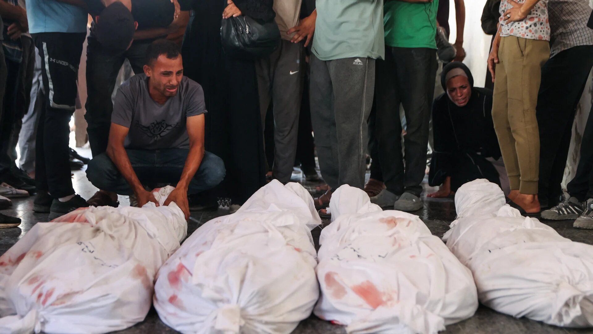 Palestinians mourn by the shrouded bodies of loved ones killed in Israeli strikes in the al-Zeitoun neighbourhood of Gaza City, ahead of their funeral at al-Ahli Arab hospital, 19 August 2025 (Omar al-Qattaa/AFP)