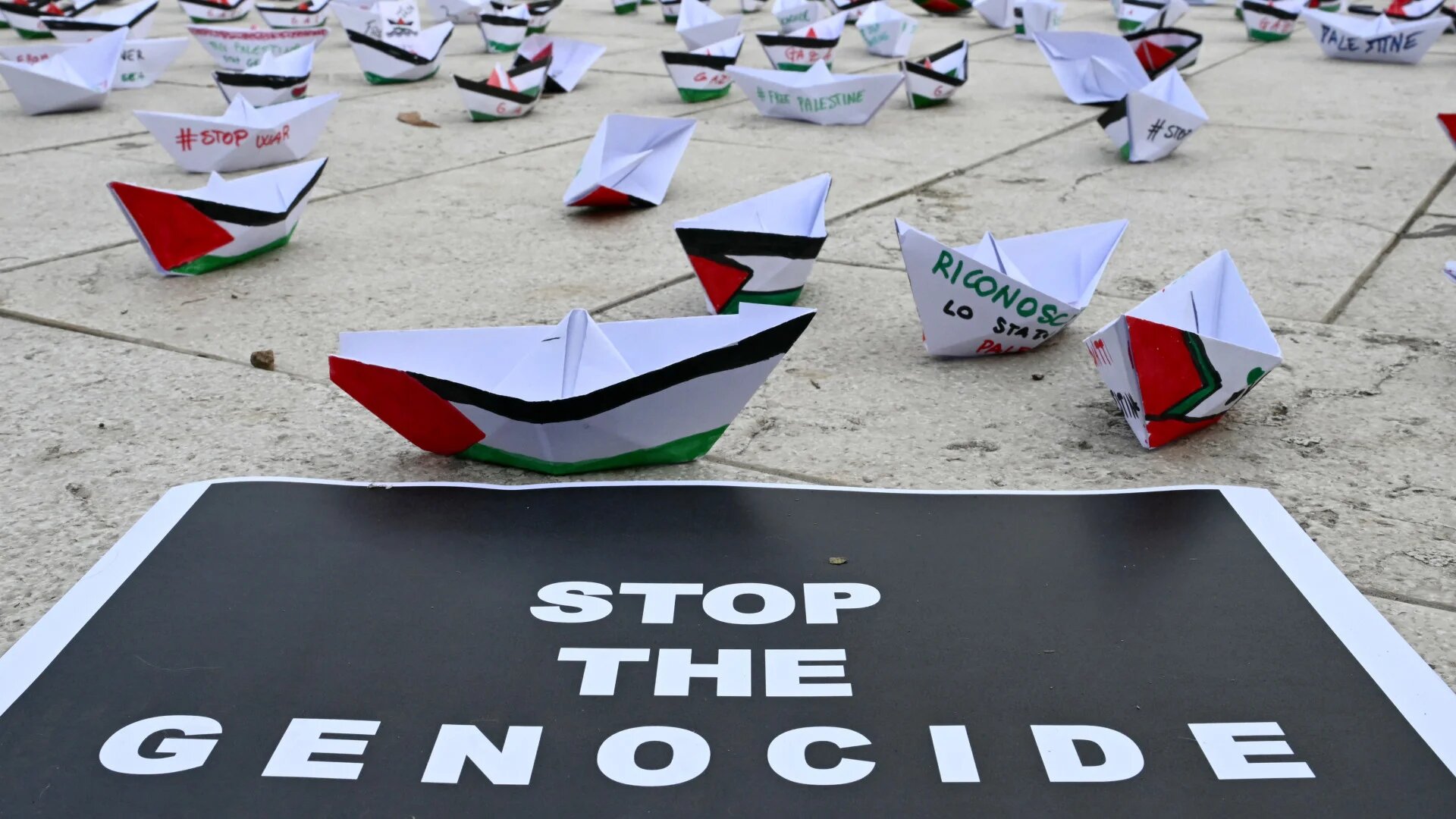 Paper boats and a 'Stop the genocide' poster at a Palestine solidarity protest during the Venice Film Festival, 30 August 2025 (Stefano Rellandini/AFP)