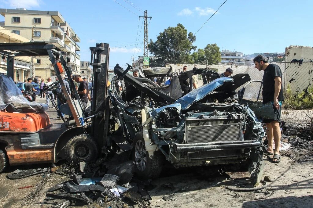 People gather around a destroyed car targeted in an Israeli drone attack in the southern Lebanese village of Zebdine, on October 6, 2025. (AFP)
