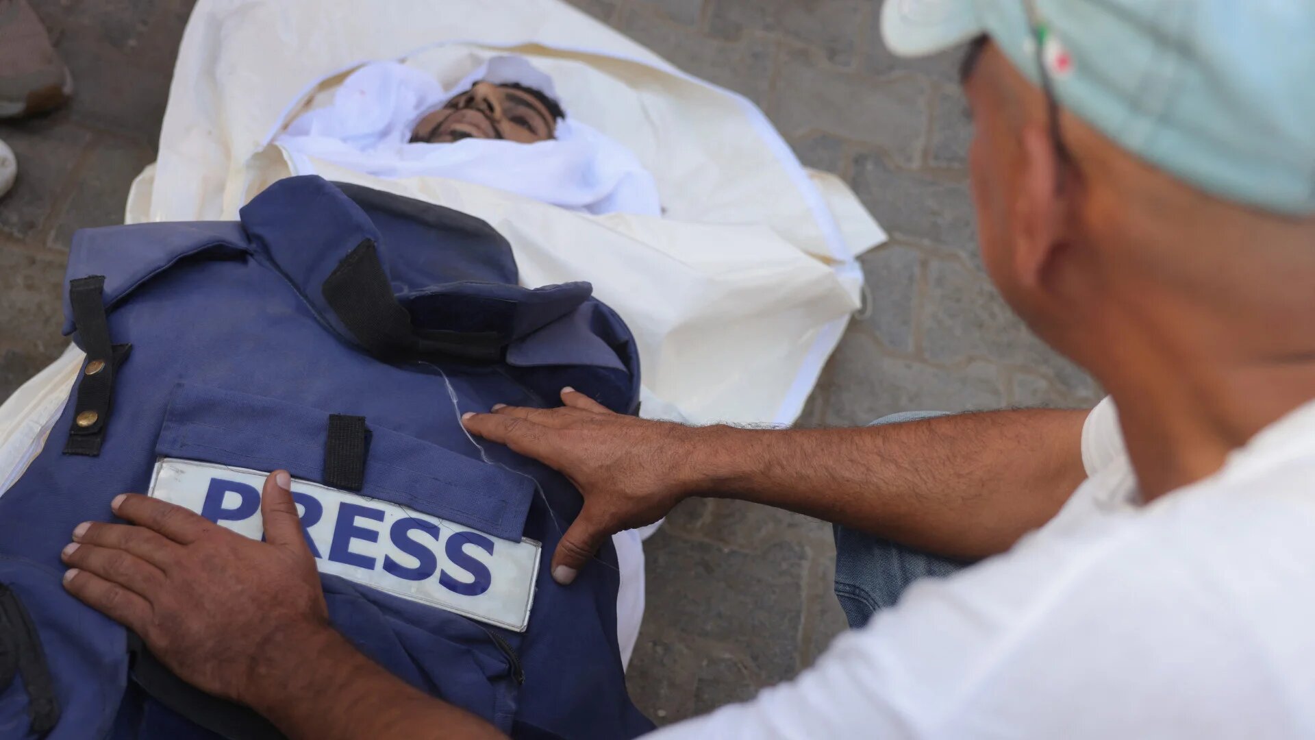 A man places the bullet-proof press vest of Palestinian journalist Ahmad Abu Mteir, killed in an Israeli strike on a house used by journalists in the central Gaza town of Zuwaida, on his draped body during preparations for his burial at Shuhada al-Aqsa Hospital in Deir al-Balah on 20 October 2025 (Bashar Taleb/AFP)