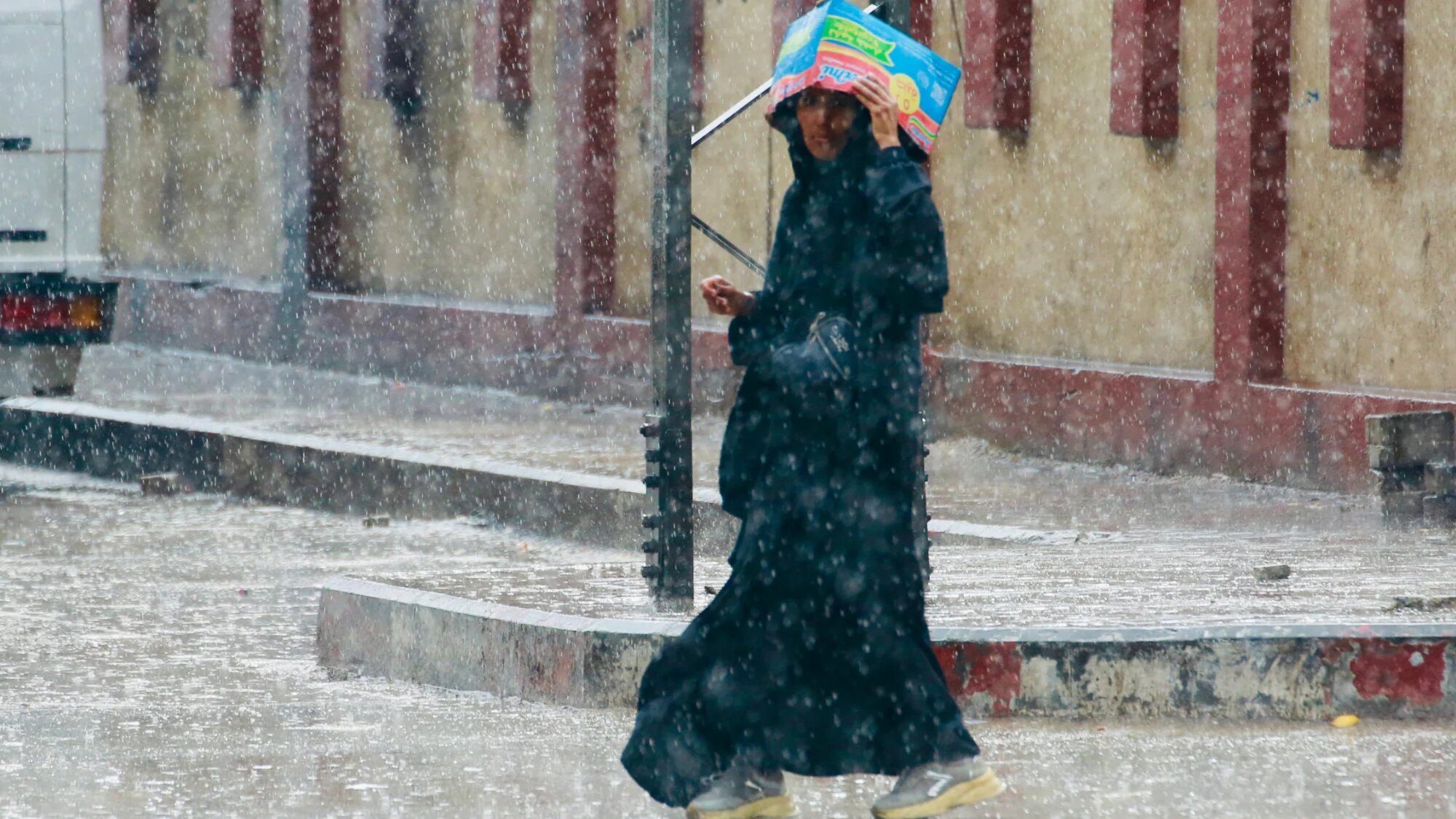 A Palestinian woman covers her head with a cardboard box as she walks under the rain in Deir al-Balah, in the central Gaza Strip on 25 November 2025 (AFP.Bashar Taleb)