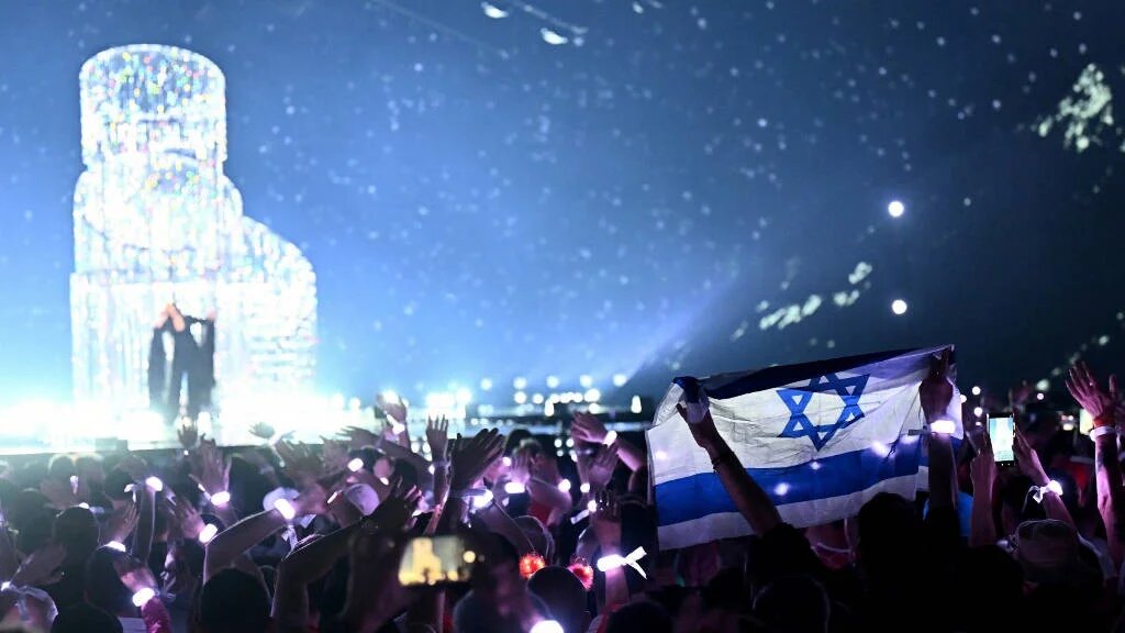 A member of the public waves Israel's national flag while watching Israeli singer Yuval Raphael representing Israel with the song "New Day Will Rise" performing during the second semi-final of the Eurovision Song Contest 2025