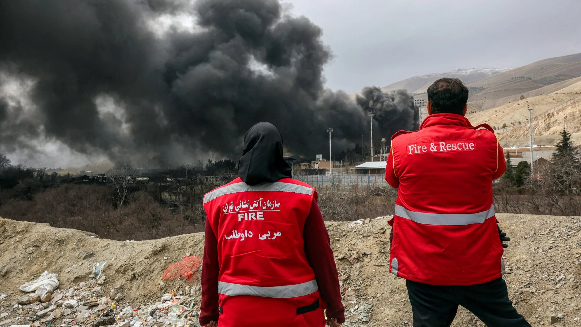 Iranian civil defence members watch smoke rise from a fire following an overnight airstrike on the Shahran oil refinery in northwestern Tehran, Iran, 8 March 2026 (AFP)