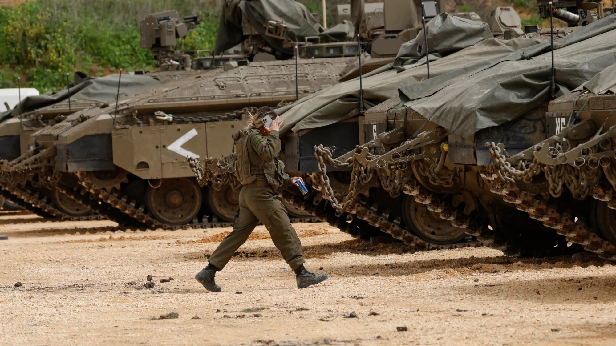 A female Israeli soldier walks towards army tanks gathered in the upper Galilee near the Israel-Lebanon boundary on 14 March 2026 (Jalaa Marey/AFP)
