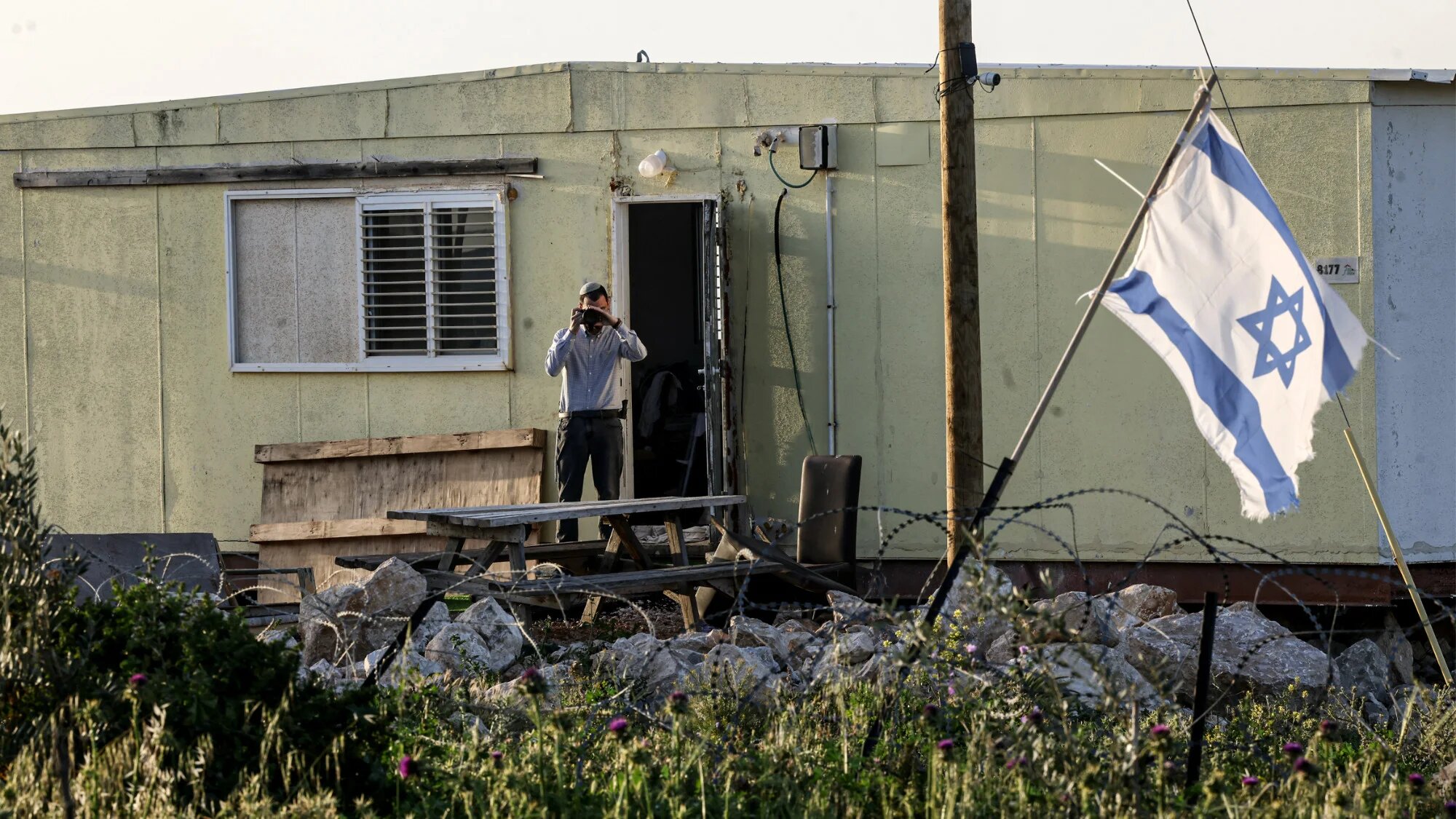 An Israeli settler at the Karmel outpost records activity in the Palestinian village of Um el-Kheir, south of Yatta in the occupied West Bank, 14 April 2026 (Hazem Bader/AFP)
