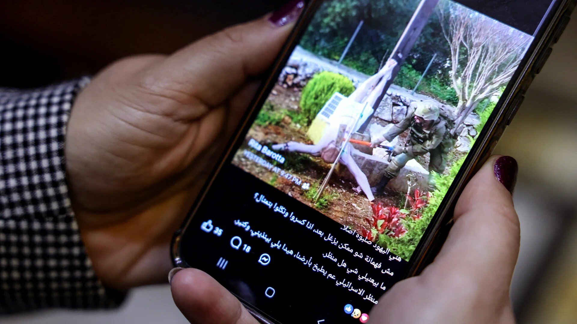 A woman in Beirut views a social media post showing an Israeli soldier striking a statue of Christ in the southern Lebanese village of Debel on 20 April 2026 (Anwar Amro/AFP)