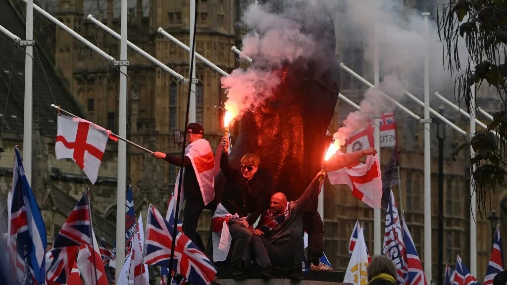In Parliament Square, supporters of British far-right activist Tommy Robinson, real name Stephen Yaxley-Lennon, let off flares beside the statue of Winston Churchill after a march organised by Unite The Kingdom in central London on May 16, 2026.