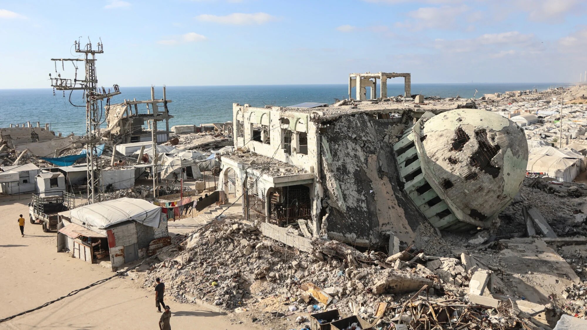 Displaced Palestinians walk past destroyed buildings and makeshift shelters near the al-Shati refugee camp, west of Gaza City, on 1 July 2026 (Omar  al-Qattaa/AFP)
