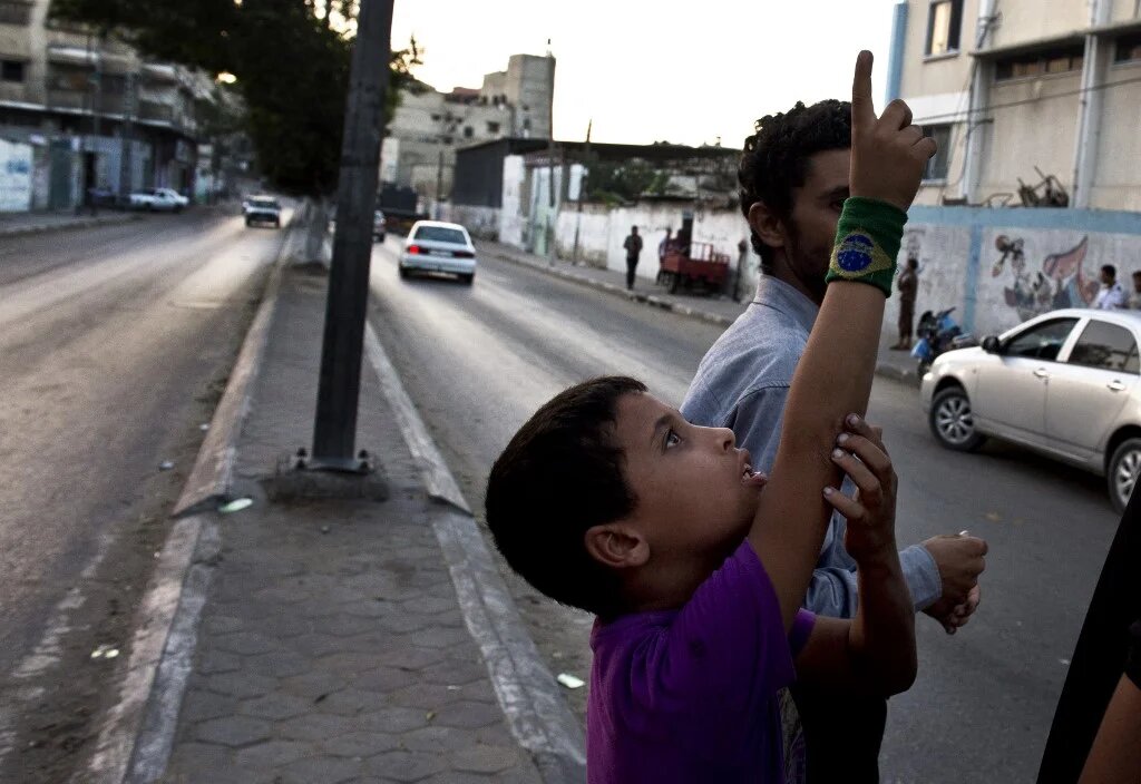 Un garçon palestinien pointe son doigt vers le ciel afin de montrer deux drones israéliens survolant l’enclave palestinienne de Gaza (AFP/Roberto Schmidt) 