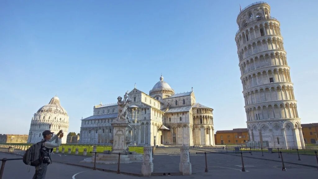 A tourist takes a photo at sunrise on May 8, 2011 of the leaning tower of Pisa in an empty square. 