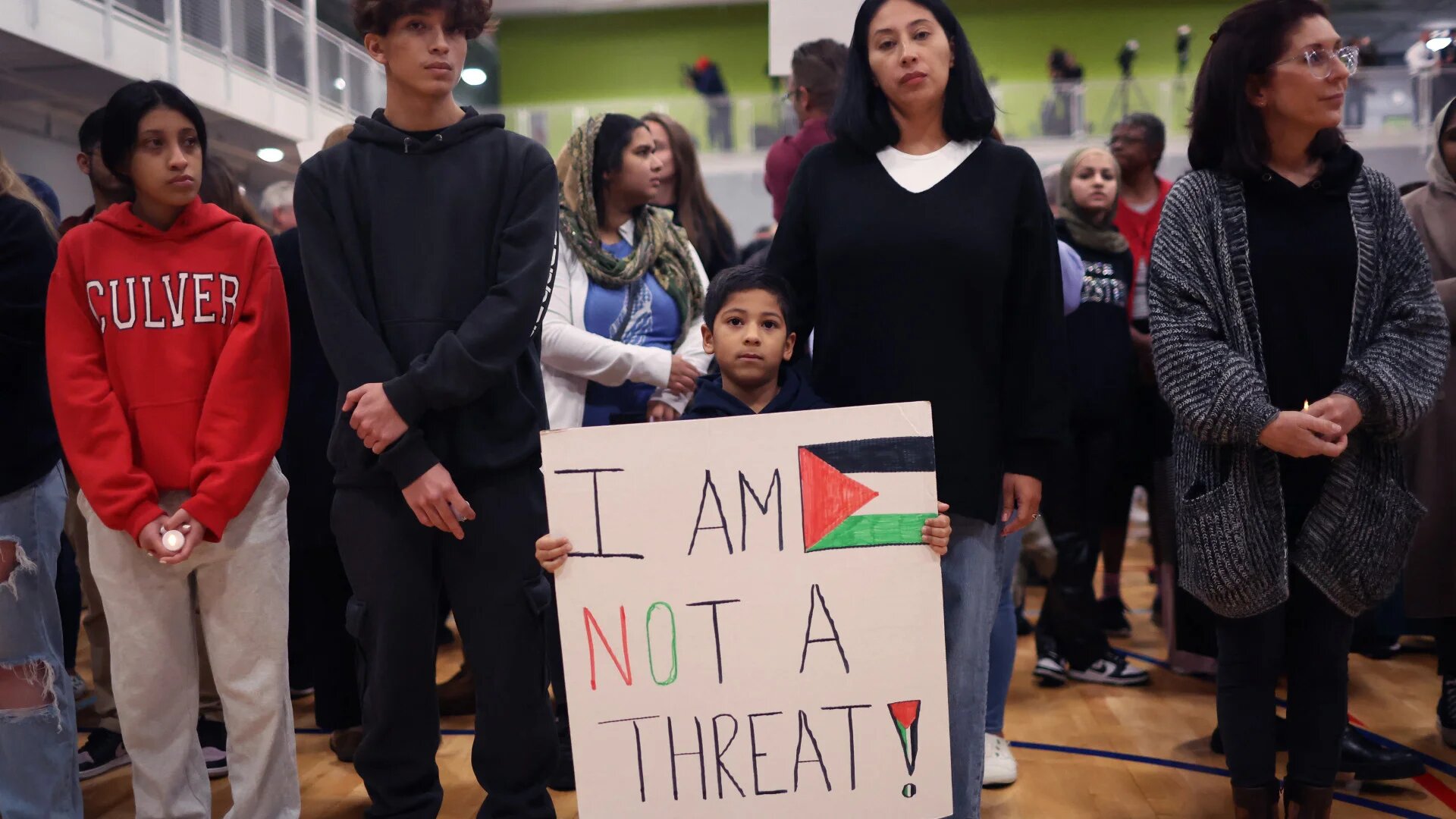 Community members, including a child carrying a sign proclaiming 'I am not a threat', attend a vigil for six-year-old Palestinian-American Wadea Al-Fayoume, who was killed in a stabbing attack fuelled by Islamophobia, on 17 October 2023 in Plainfield, Illinois (Scott Olson/AFP)