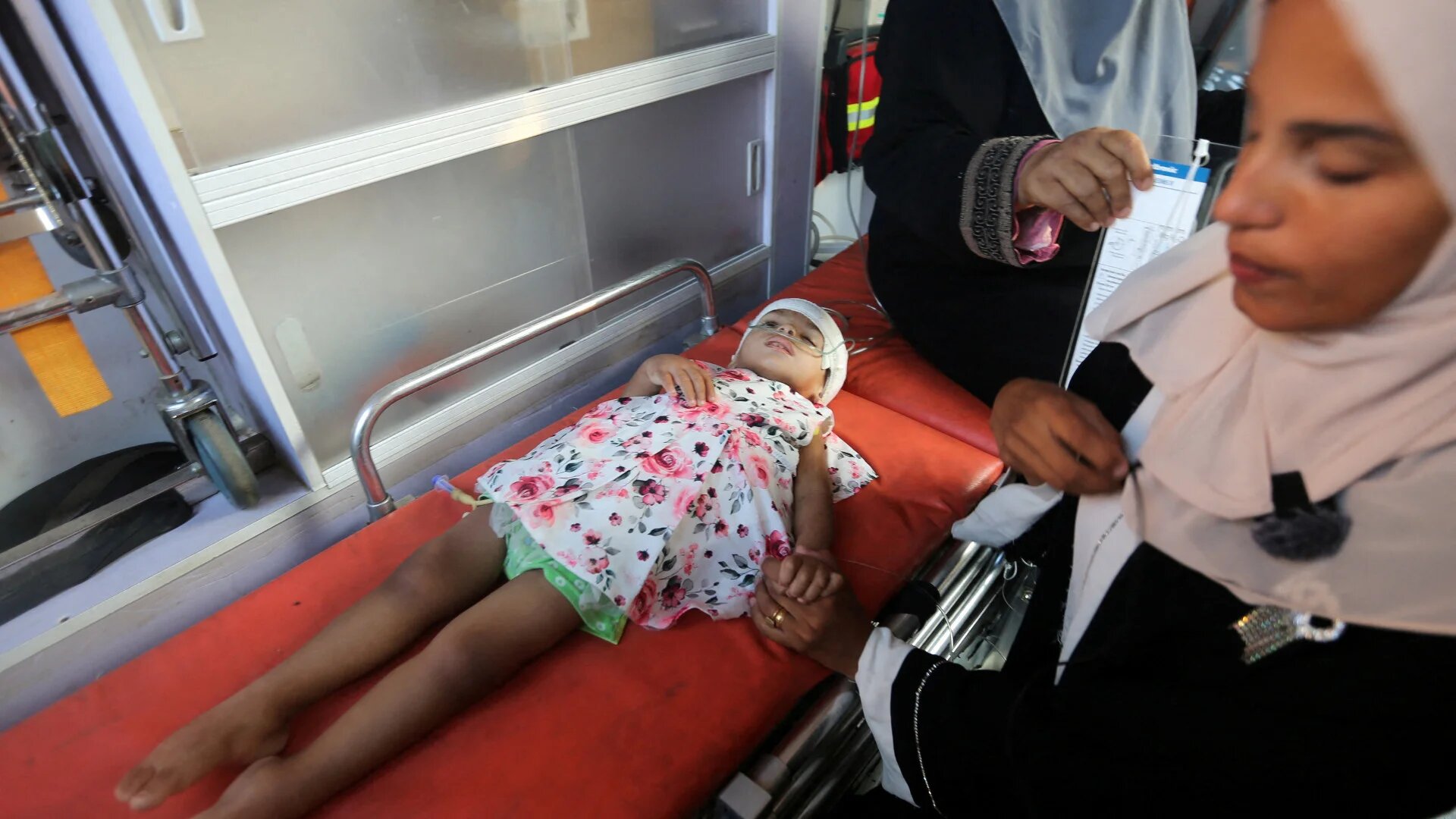 A Palestinian woman holds a child's hand as cancer patients wait to leave Gaza for treatment abroad, amid the Israel-Hamas conflict, in Khan Younis, in the southern Gaza Strip, on 15 August 2024 (Hatem Khaled/Reuters)