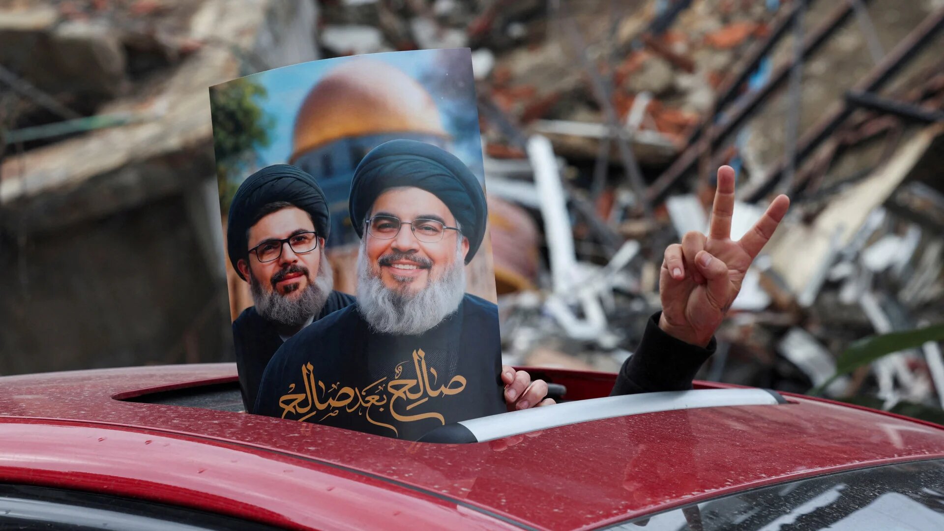 A victory sign and a poster with an image of late Hezbollah leader Sayyed Hassan Nasrallah and late senior Hezbollah official Hashem Safieddine is seen from the opening of a car in Beirut's southern suburbs, after a ceasefire between Israel and Hezbollah took effect on 27 November (Reuters/Mohamed Azakir)