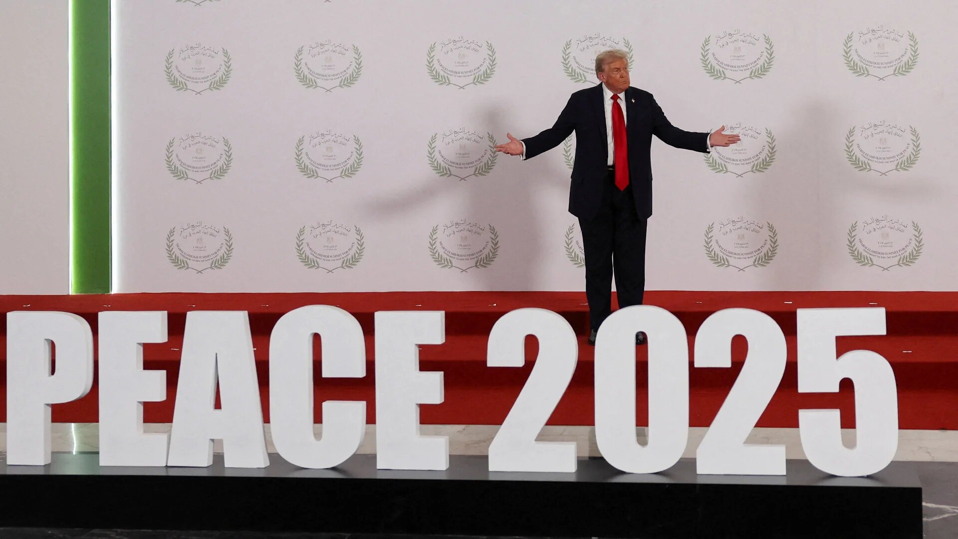 US President Donald Trump poses next to a 'Peace 2025' sign during a summit on ending the Gaza war in Sharm el-Sheikh, Egypt, on 13 October 2025 (Suzanne Plunkett/ Pool/Reuters)