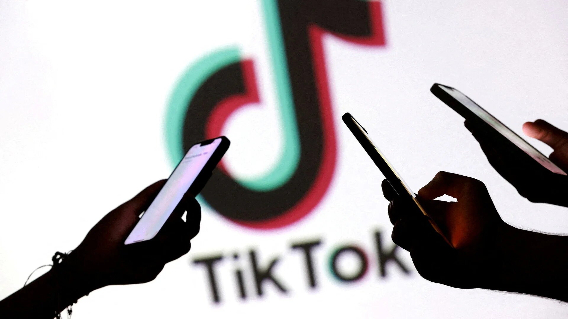 Teenagers pose for a photo while holding smartphones in front of a TikTok logo in this illustration taken on 11 September 2025 (Dado Ruvic/Reuters)