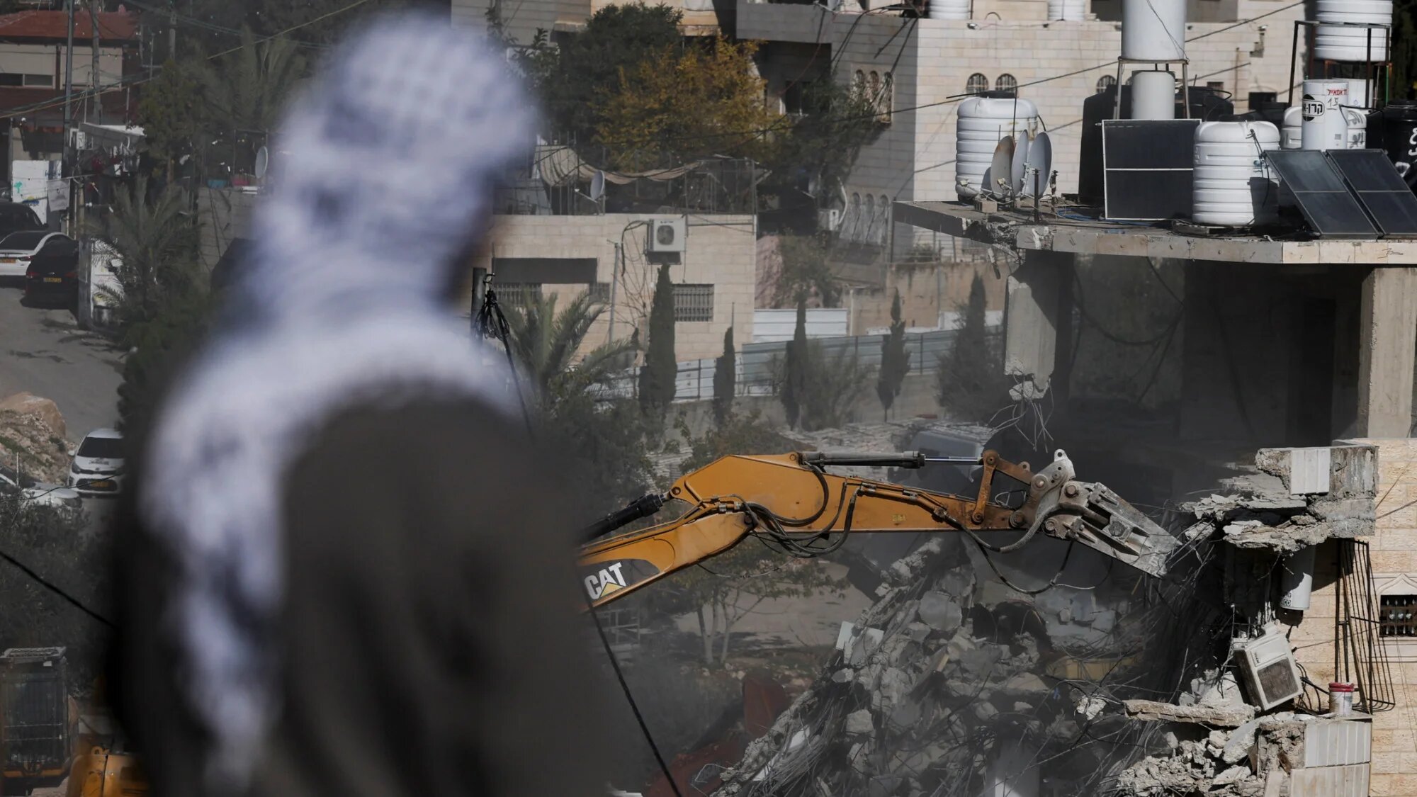A man watches as Israeli forces demolish Palestinian homes near the Silwan neighbourhood in occupied East Jerusalem on 22 December 2025 (Ammar Awad/Reuters)