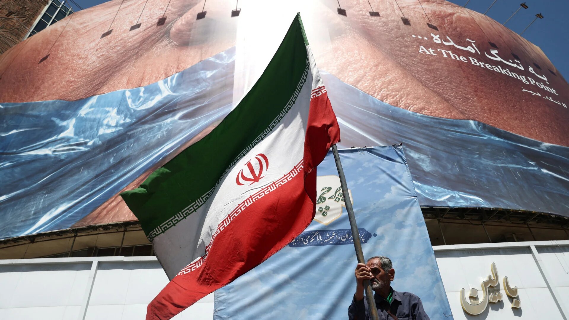 A man holds an Iranian flag near an anti-US billboard depicting US President Donald Trump and the Strait of Hormuz in Tehran on 30 May 2026 (Majid Asgaripour/WANA via Reuters)