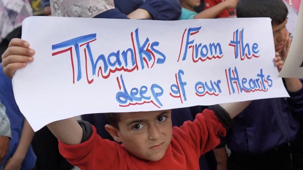 A Palestinian child holds a sign thanking pro-Palestinian student solidarity initiatives in the US and Canada, in Deir el-Balah in the central Gaza Strip, 1 May 2024 (AFP)