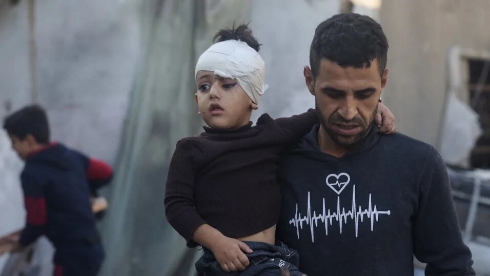 A Palestinian man carries a child injured during Israeli bombardment in Rafah, in the southern Gaza Strip, 2 December 2023 (Mohammed Abed/AFP)