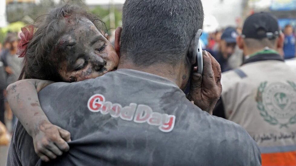 A Palestinian man covered with dust carries an injured baby girl into the al-Shifa hopsital in Gaza City following Israeli strikes on 29 October 2023 (AFP)