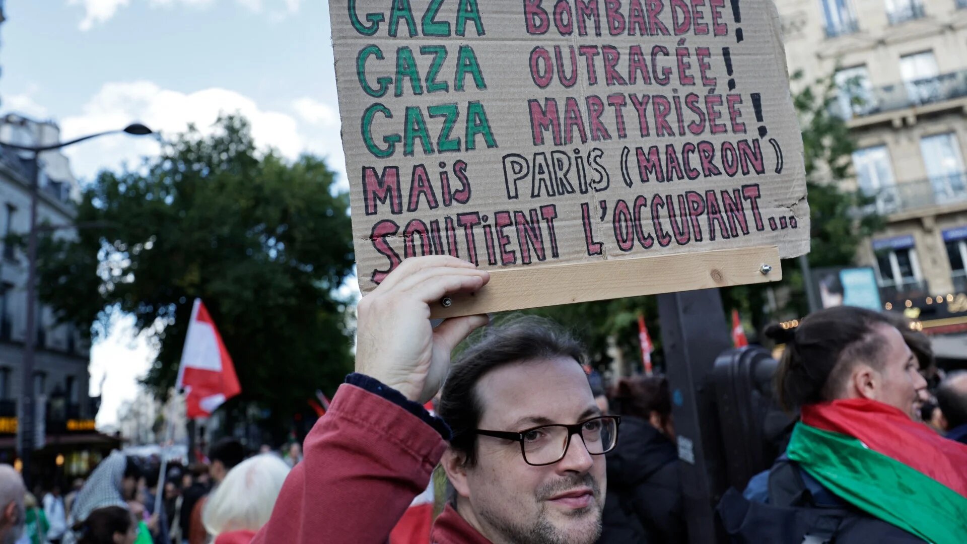 A man holds a placard reading in French 'Gaza bombarded, but Paris (Macron) supports the occupier' at a rally in Paris, on 5 October 2024 (AFP)