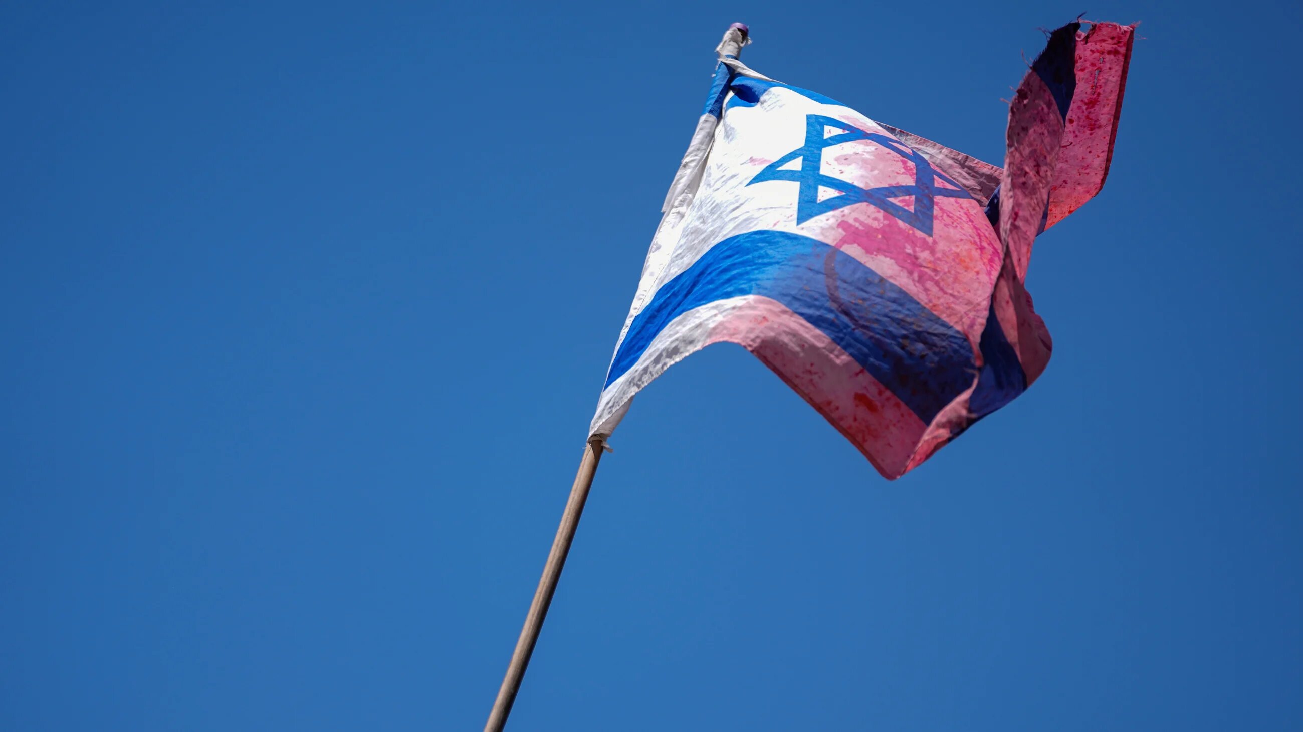 A demonstrator waves a coloured Israeli flag during a protest against the government plan to overhaul the judicial system, outside Israel's parliament in Jerusalem24 July 2023 (AP)