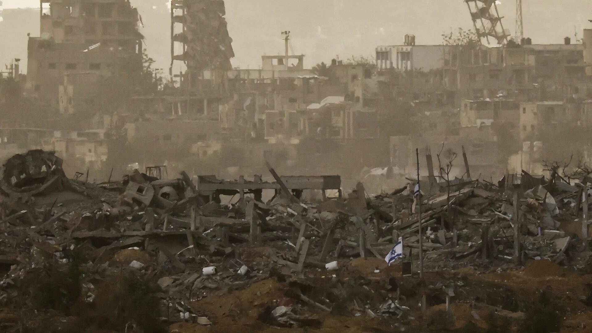 An Israeli flag planted by Israeli forces flies among debris in northern Gaza following Israeli bombardment on 12 December 2023 (Clodagh Kilcoyne/Reuters)