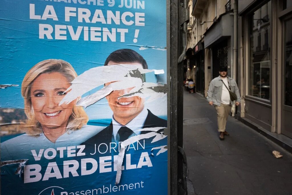 A man walks past an electoral poster of the National Rally (RN) with defaced portraits of party president Jordan Bardella (R) and leader of parliamentary group Marine Le Pen (L), in Paris on 10 June (Joel Saget/AFP)