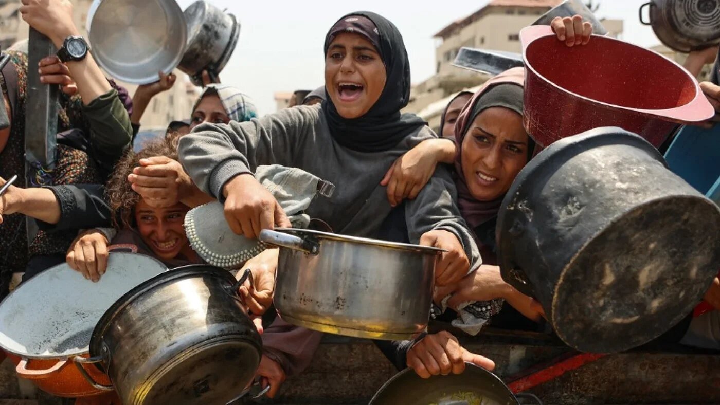 Palestinians gather to receive cooked meals from a food distribution centre in Gaza City on 13 August (AFP)