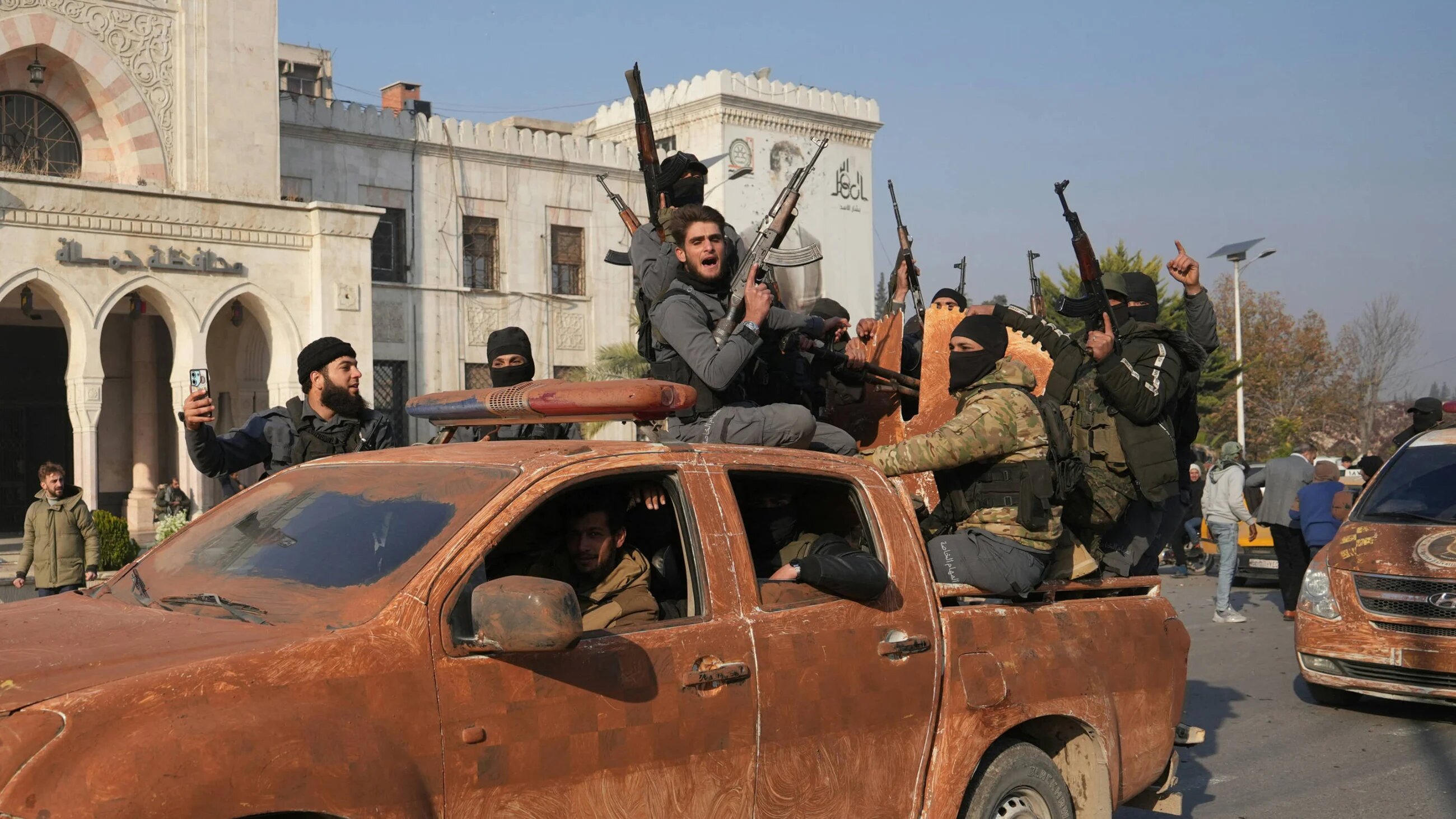 Syrian anti government fighters celebrate as they pour into the captured central-west city of Hama on 6 December 2024 (AFP)