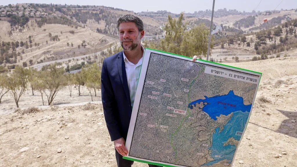 Israeli far-right Finance Minister Bezalel Smotrich holds a map of an area near the settlement of Maale Adumim, a land corridor known as E1, outside Jerusalem in the occupied West Bank, on August 14, 2025 (Menahem Kahana / AFP)