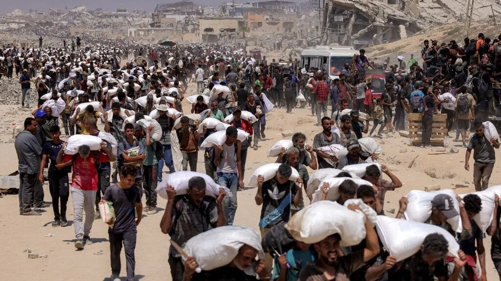 Palestinians walk with sacks of flour delivered after trucks carrying humanitarian aid entered northern Gaza on 27 July 2025 (AFP/Bashar Taleb)