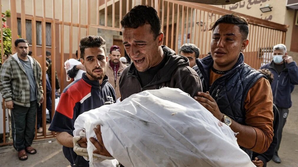 A Palestinian man mourns over the body of a relative killed in an Israeli strike at the Nasser hospital in Khan Younis, southern Gaza Strip, 28 December 2023 (AFP)