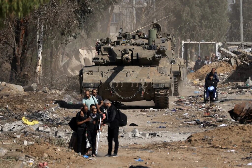 Palestinians pass an Israeli tank as they flee northern Gaza on the southern outskirts of Gaza City, during a four-day truce, on 24 November 2023 (AFP)