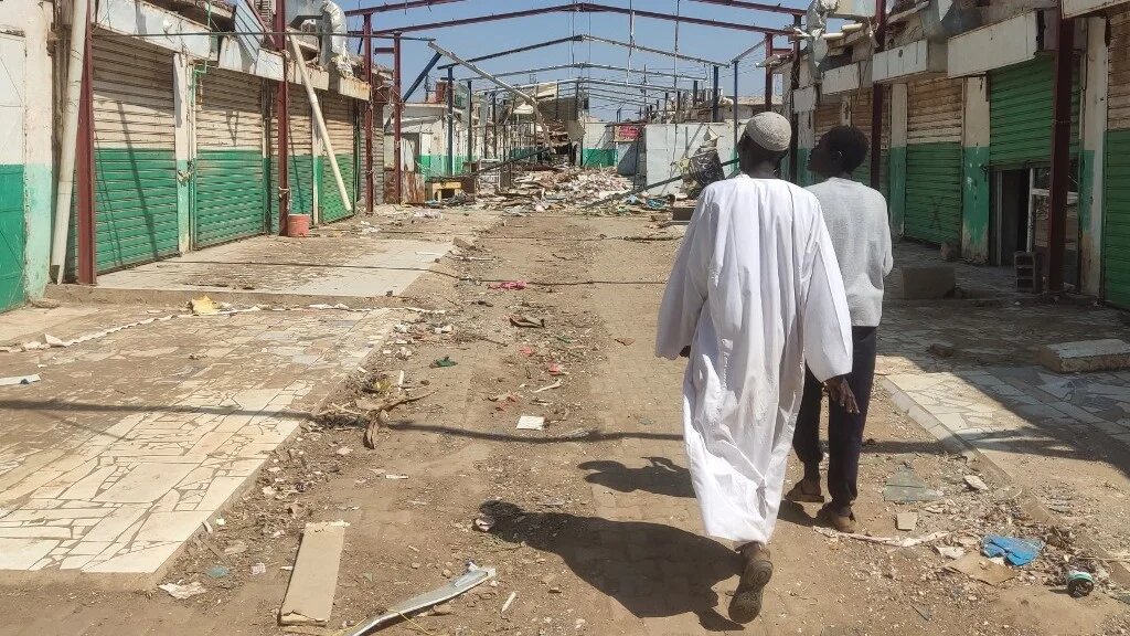 People walk past damaged buildings in Wad Madani, which was retaken by the Sudanese army a month earlier, in Sudan's al-Jazira state on 11 February 2025 (AFP)