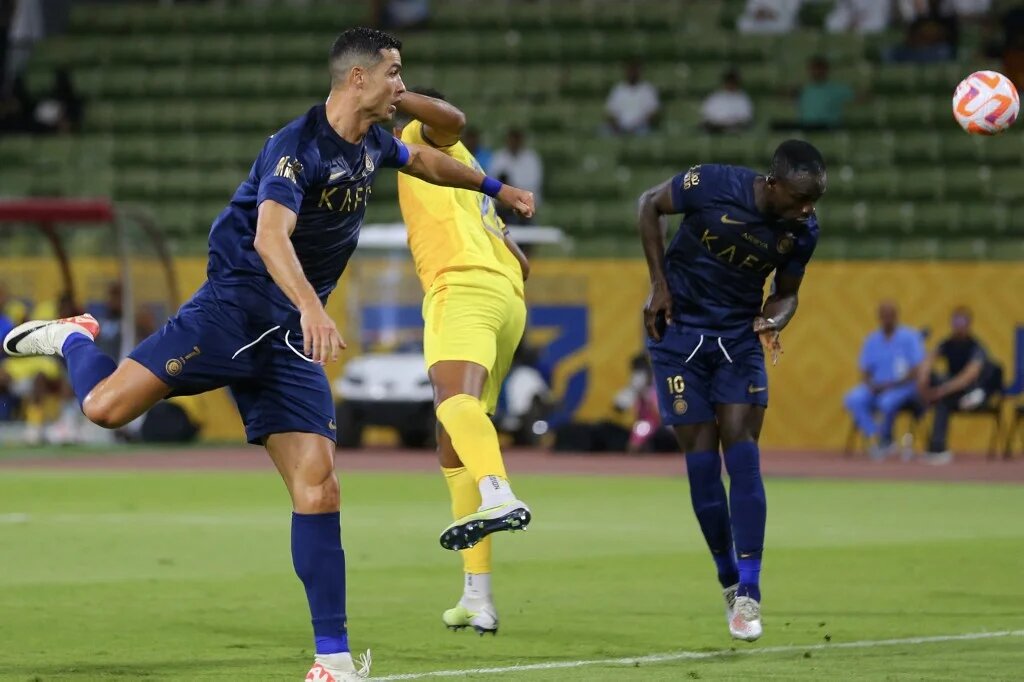 Al-Nassr's Sadio Mane (R) heads the ball as teammate Cristiano Ronaldo (L) looks on during the Saudi Pro League match against Al-Hazem at the King Abdullah Sports City, Buraidah, 2 September 2023 (AFP)