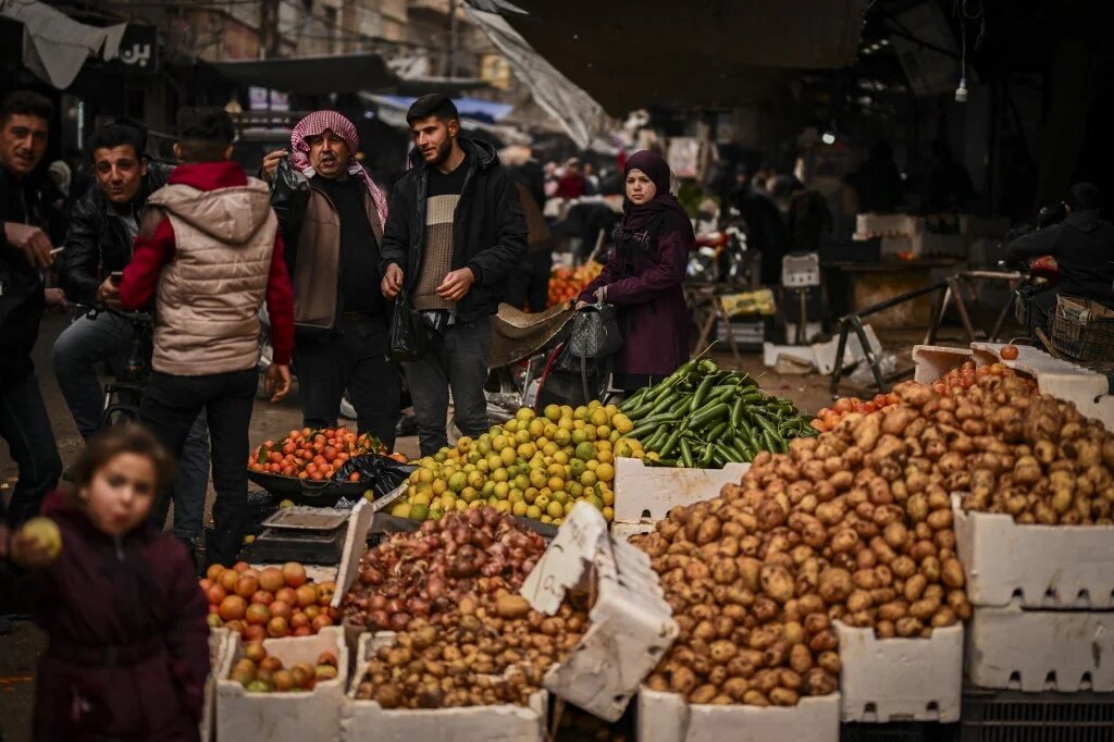 People walk past stalls at a street market in the town of Douma, on the outskirts of the Syrian capital Damascus on December 21, 2024. (Aris Messinis /AFP)