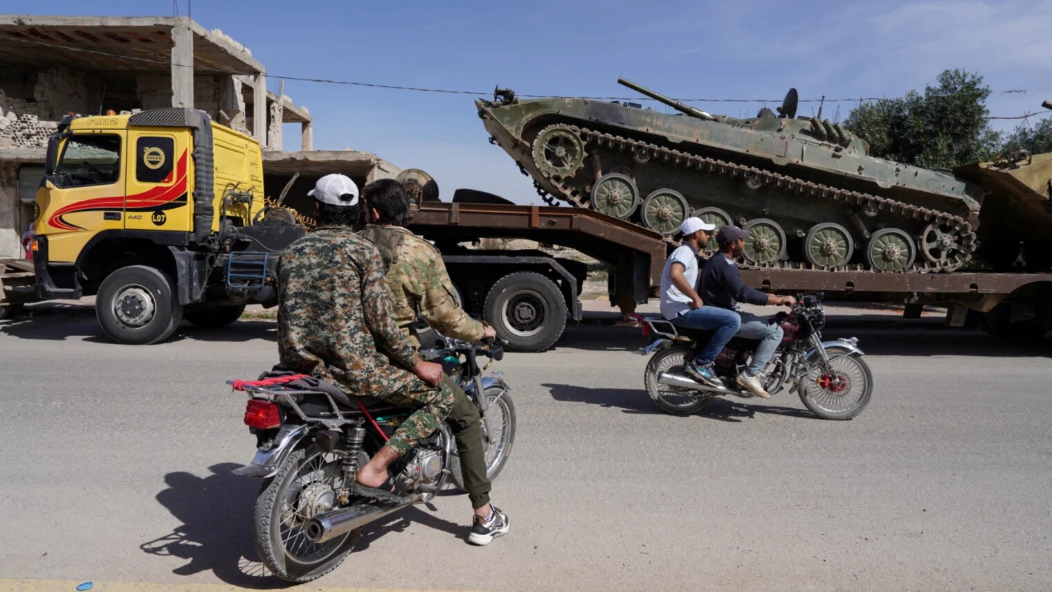 Men pass on motorbikes as Syrian troops tow military vehicles towards the Syrian-Lebanese border following clashes with Lebanese soldiers, in Qusayr, Syria, 17 March 2025 (Karam al-Masri/Reuters)
