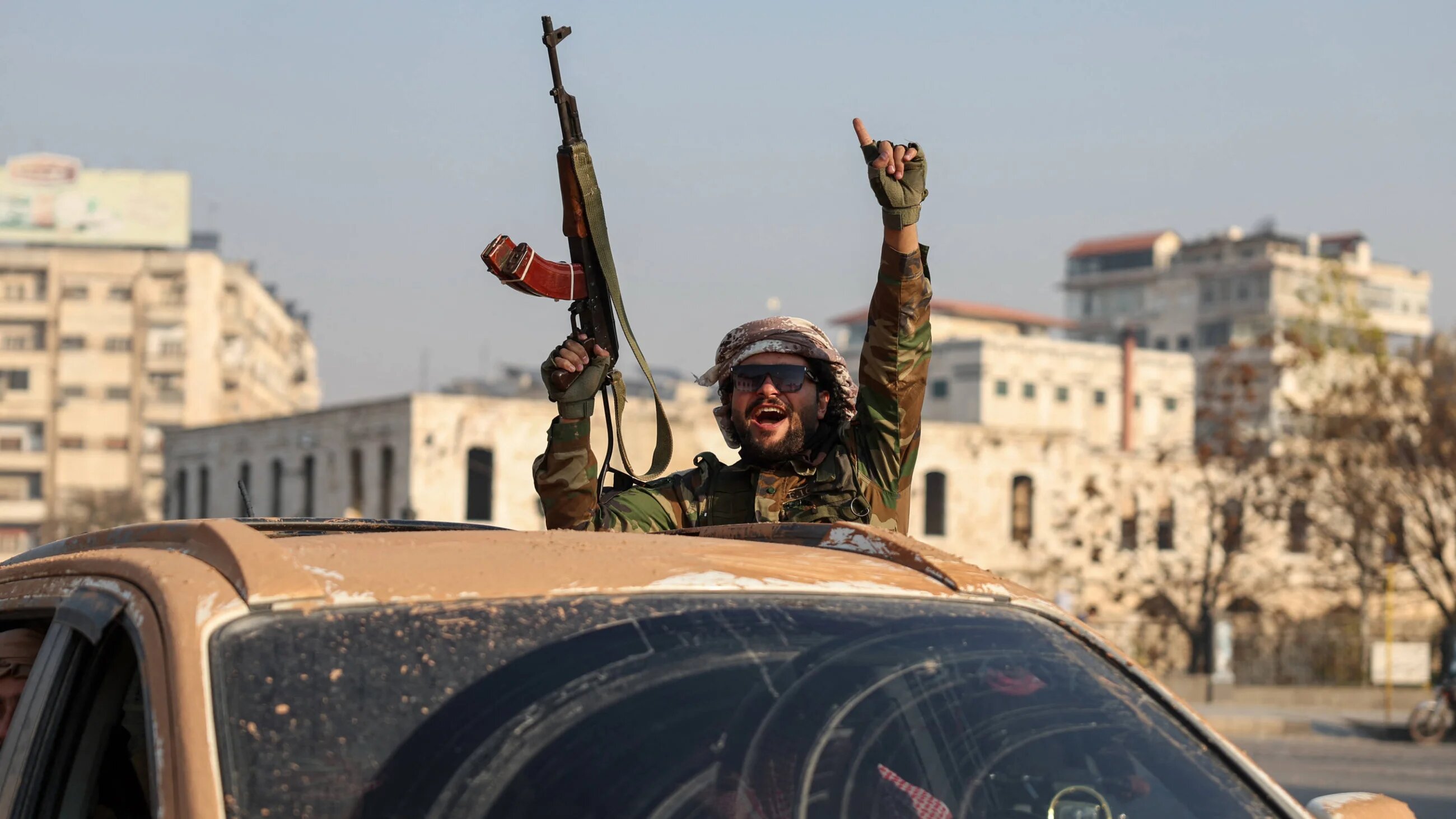 An anti-government fighter gestures from inside a vehicle patrolling the streets of Hama after they captured the central Syrian city, on 6 December 2024 (AFP)