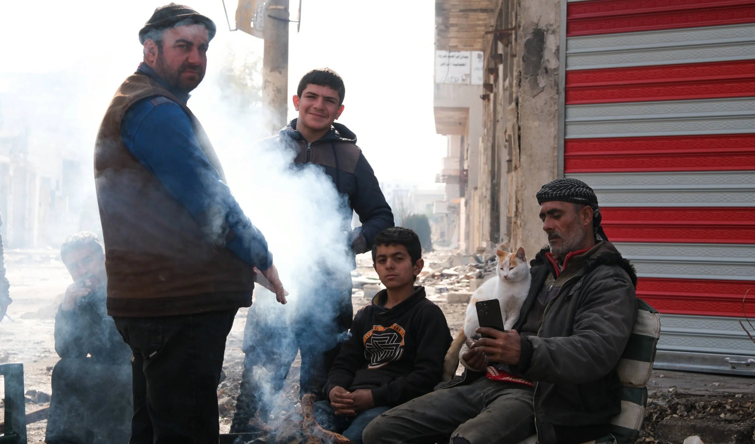 Syrians who have returned to Saraqib to reclaim their homes warm themselves on a brazier in the centre of town, 31 December 2024 (Andrew Waller/MEE)  
