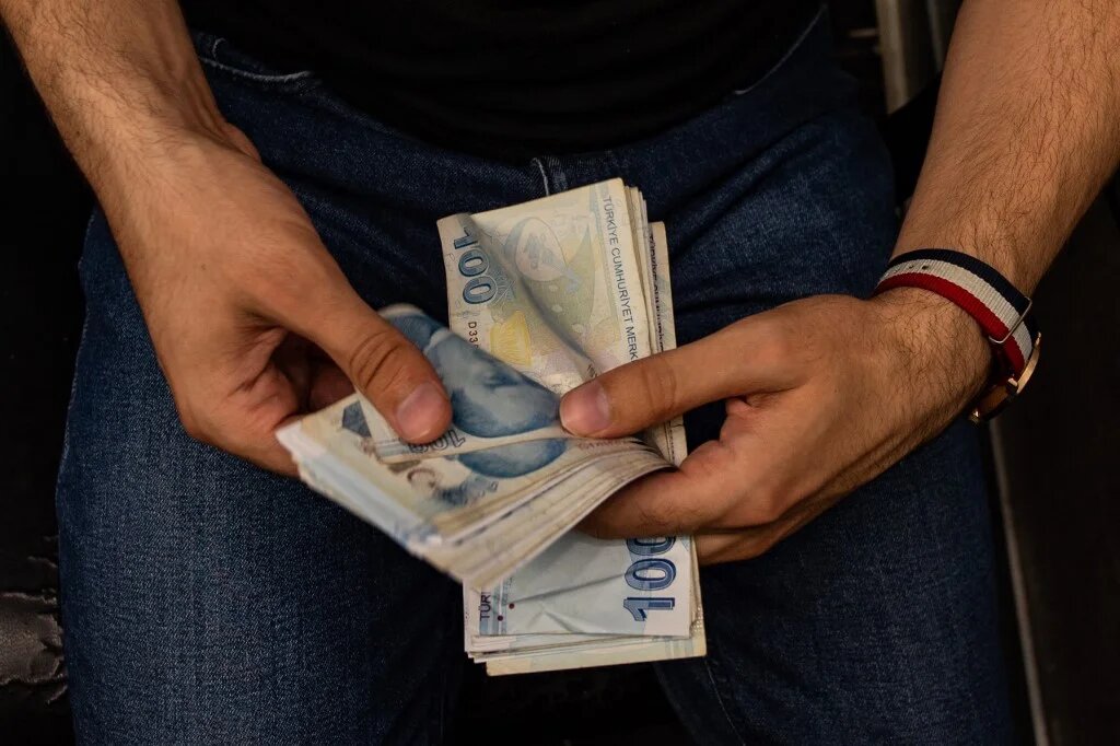 A currency exchange office worker counts Turkish Lira banknotes in front of the electronic panel displaying currency exchange rates at an exchange office in Istanbul, on August 6, 2020  (Yasin Akgul / AFP)