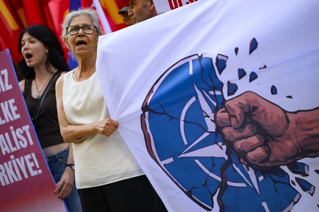 A protestor hold a banner bearing the NATO logo being destructed by a punch during an anti-NATO demonstration in Istanbul, ahead of a NATO summit, on July 5, 2026. The next NATO summit will take place in Ankara on July 7-8 and is expected to be attended by 32 leaders including US President. (Yasin AKGUL / AFP)