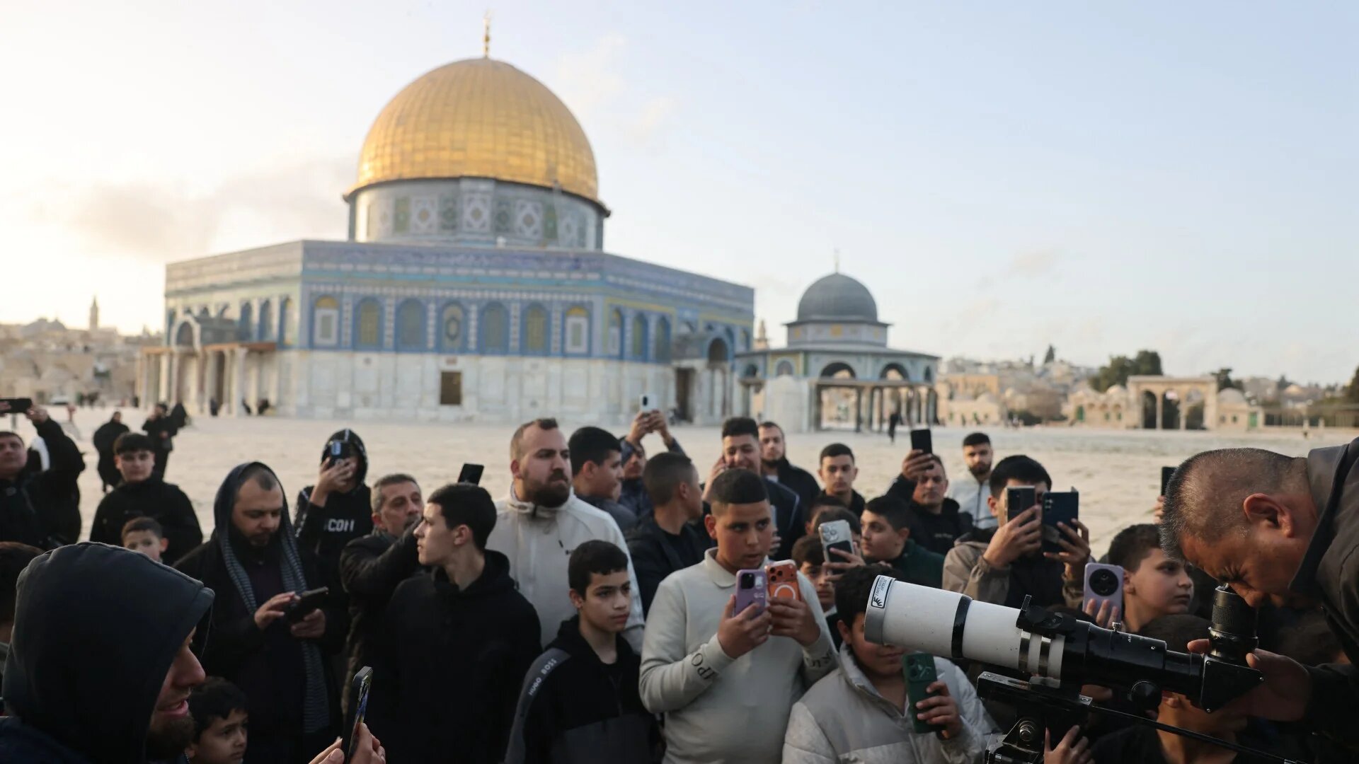 People watch as a man uses a telescope while searching for the crescent moon to mark the start of the Muslim holy fasting month of Ramadan, near the Dome of the Rock at Al-Aqsa mosque, in the Old City of Jerusalem on 17 February 2026 (AFP/Ahmad Gharabli)