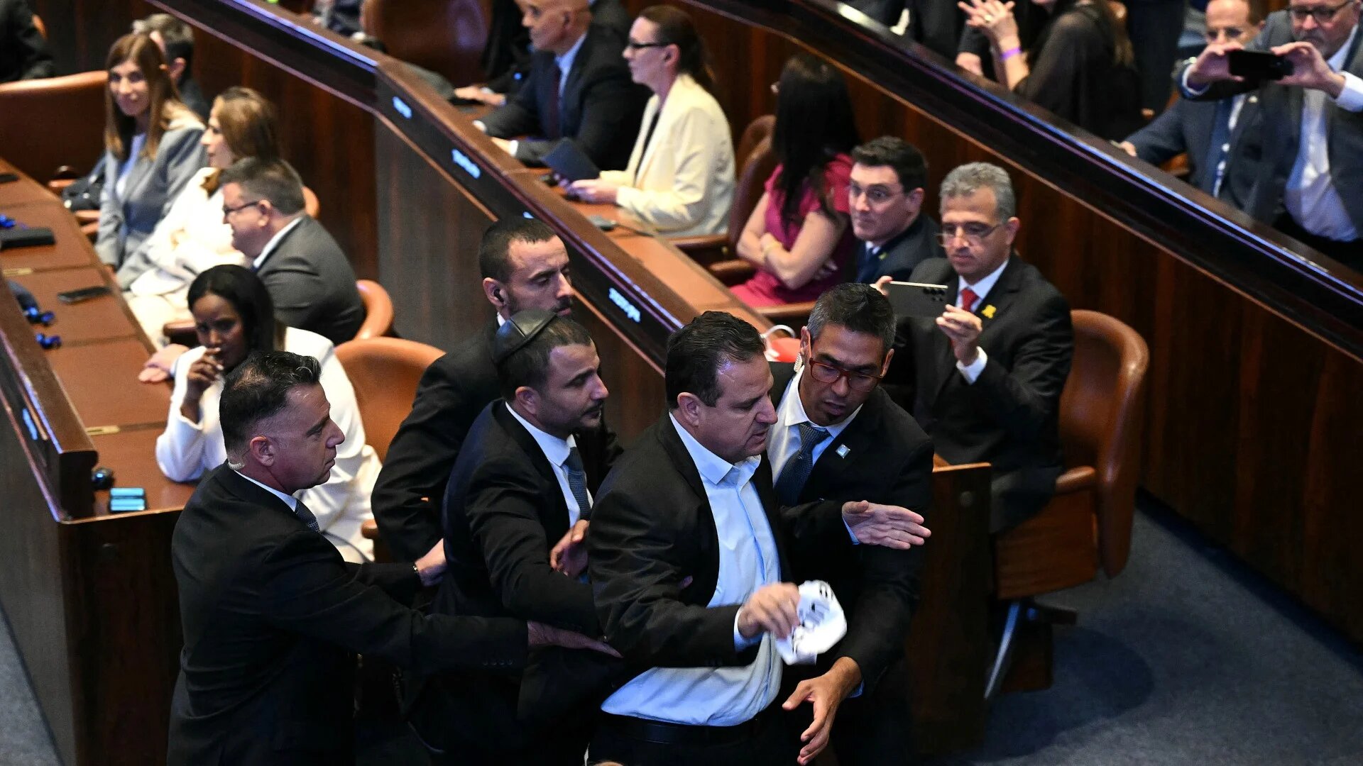 Israeli Knesset member Ayman Odeh (C) is escorted out after holding a sign reading "Recognise Palestine" during a speech by US President Donald Trump at the Israeli parliament in Jerusalem on 13 October 2025 (AFP/Pool/Saul Loeb)