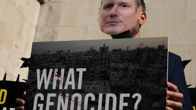 A person dressed as British Prime Minister Keir Starmer holds a placard outside the Royal Courts of Justice alongside other Pro-Palestinian activists in London on 13 May 2025 (Adrian Dennis/AFP)